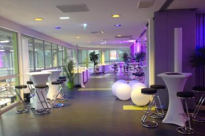 Bâtiment moderne avec façade vitrée, éclairé au crépuscule, reflété dans un plan d'eau calme.