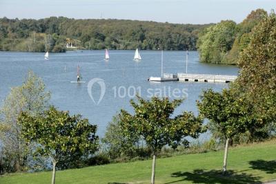 Bâtiment moderne avec façade vitrée, éclairé au crépuscule, reflété dans un plan d'eau calme.