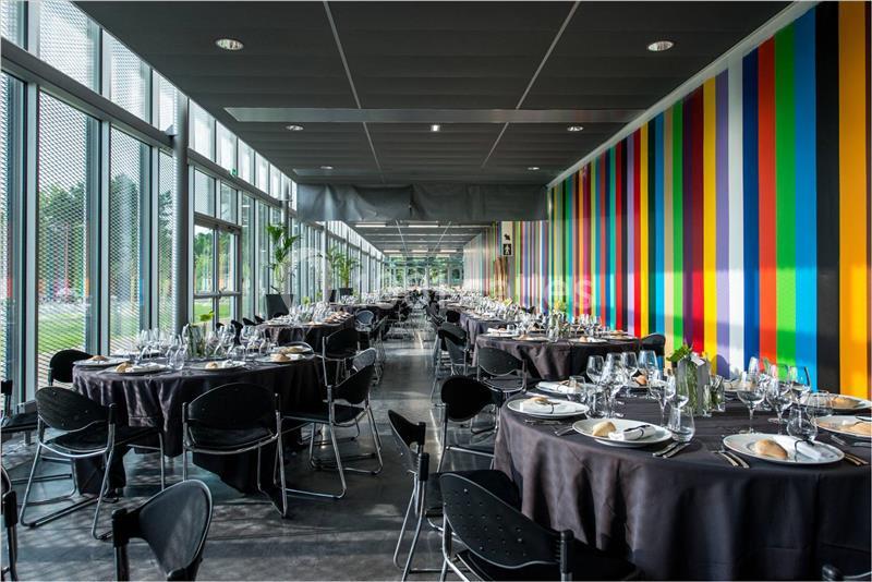 Salle de réception moderne avec tables dressées, nappes noires, vaisselle élégante et mur coloré à rayures verticales.