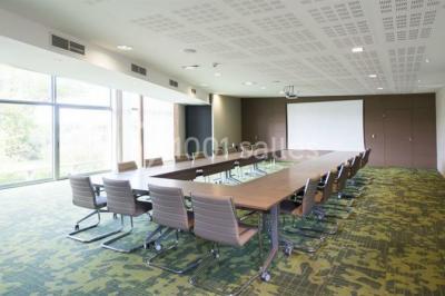 Bâtiment moderne avec façade vitrée, éclairé au crépuscule, reflété dans un plan d'eau calme.