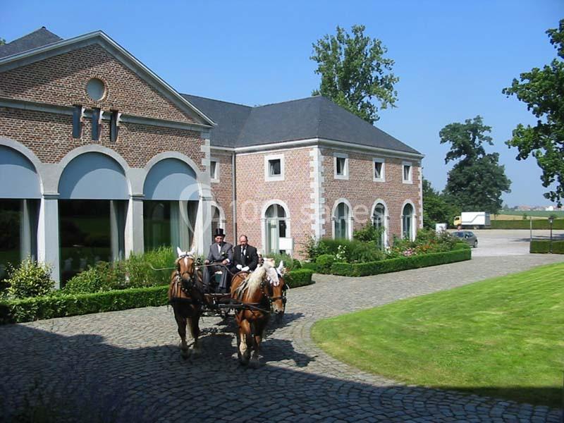 Attelage de deux chevaux tirant une calèche devant un bâtiment en briques entouré de verdure.