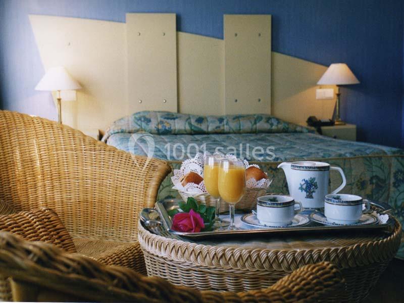 Petit-déjeuner avec jus d'orange et café servi sur un plateau dans une chambre d'hôtel avec lit et fauteuils en osier.