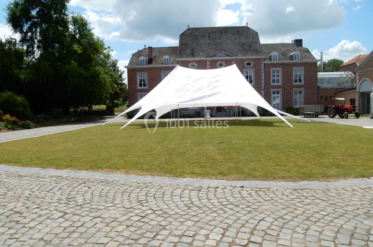 Tente blanche installée sur une pelouse devant un bâtiment en briques rouges avec des fenêtres à volets blancs.