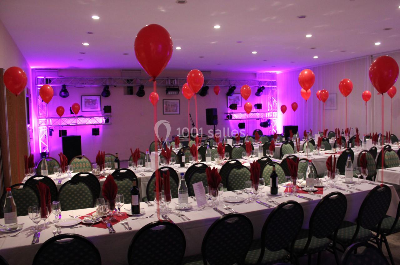 Salle de réception décorée avec des ballons rouges, tables dressées avec nappes blanches et serviettes assorties.