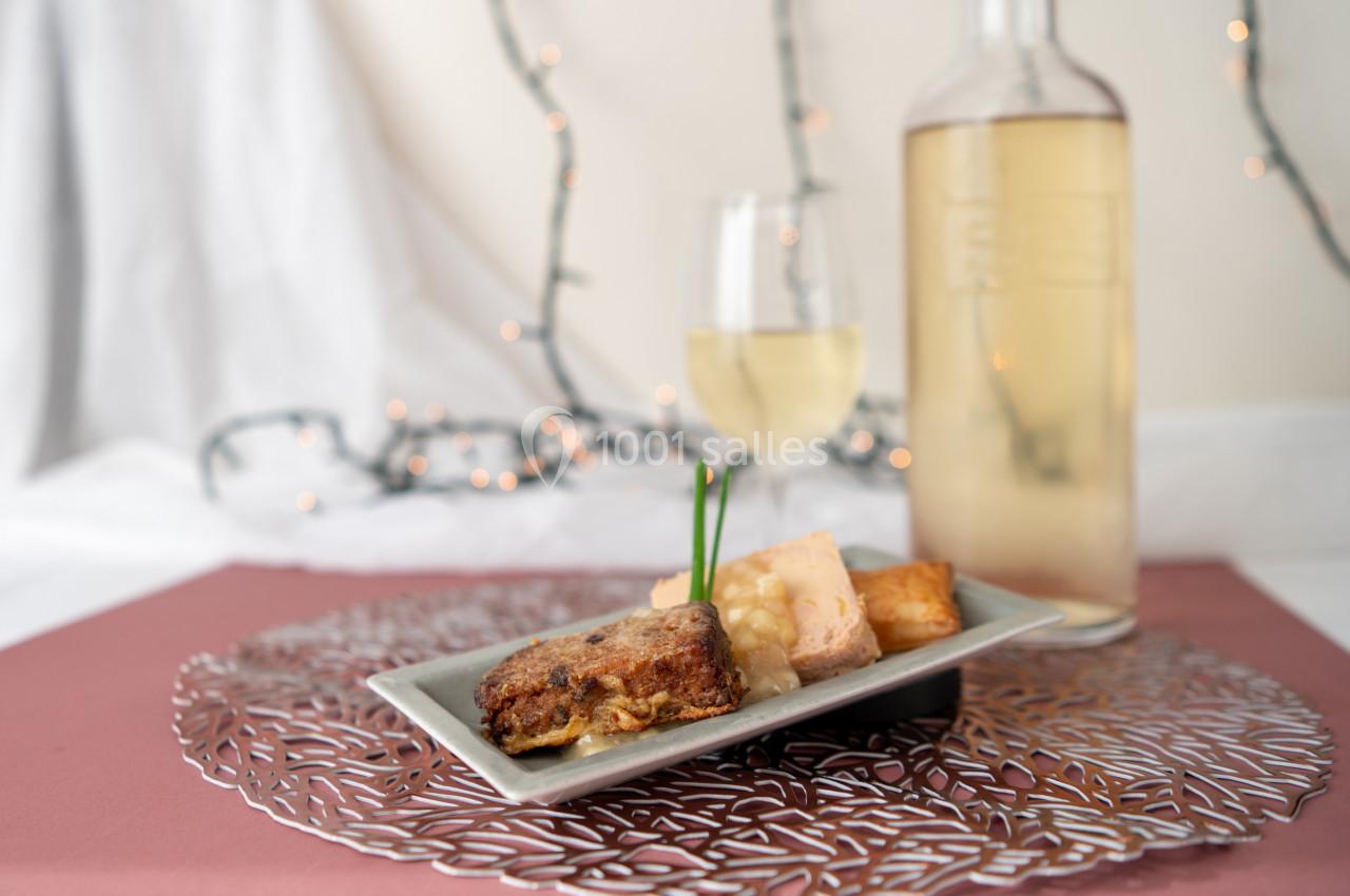 Assiette de dégustation avec foie gras, pain grillé et accompagnements, servie avec un verre et une bouteille de vin blanc.