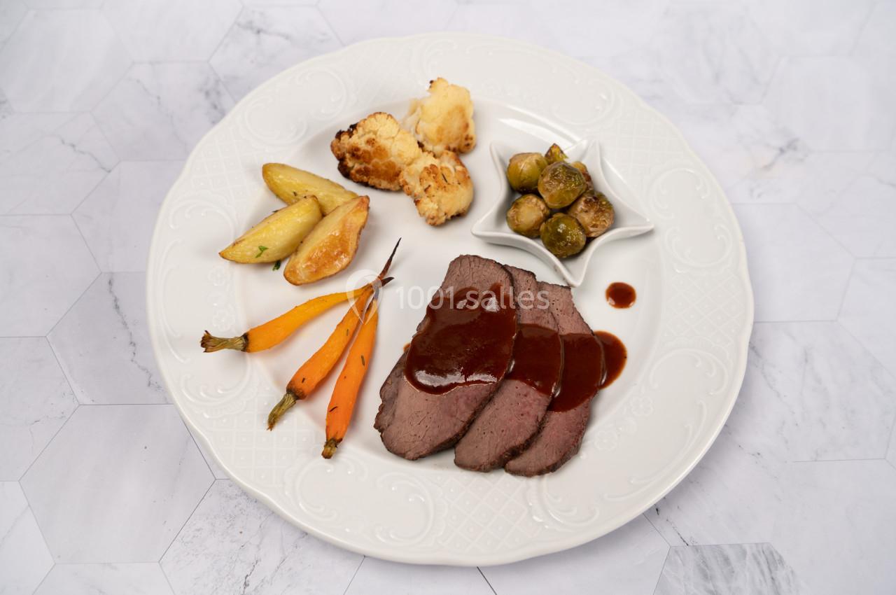 Assiette contenant des tranches de viande avec sauce, carottes, pommes de terre, choux de Bruxelles et chou-fleur rôti.