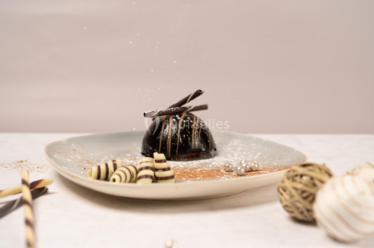 Dessert au chocolat décoré de spirales en chocolat et saupoudré de sucre glace, présenté sur une assiette beige.