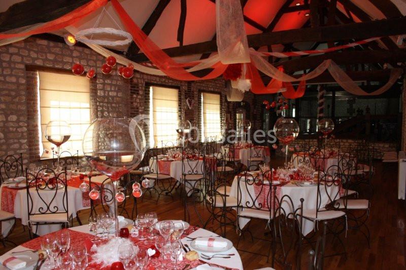 Salle décorée pour un événement avec des tables dressées, des nappes rouges et blanches, et des suspensions en tissu.