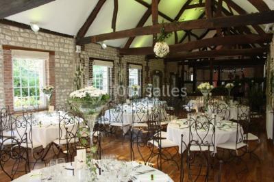 Salle de réunion avec des tables blanches, des chaises en osier et un écran de projection, dans un cadre en briques…