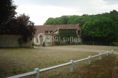 Salle de réunion avec des tables blanches, des chaises en osier et un écran de projection, dans un cadre en briques…