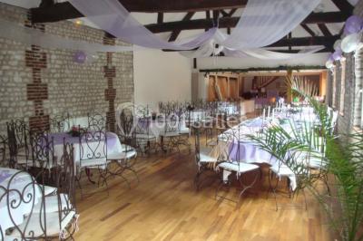 Salle de réunion avec des tables blanches, des chaises en osier et un écran de projection, dans un cadre en briques…