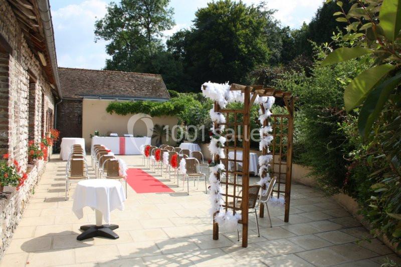 Terrasse extérieure aménagée pour une cérémonie, avec des chaises, une arche décorée et une allée rouge.