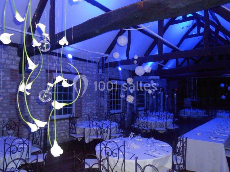 Salle de réception décorée avec des tables dressées, des guirlandes lumineuses et des suspensions florales blanches.