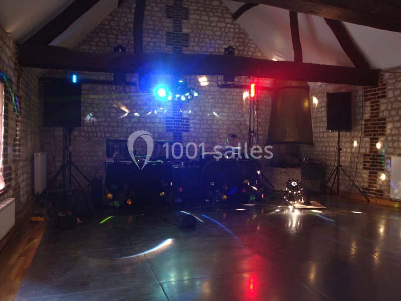 Salle en pierre avec jeux de lumière colorés, piste de danse vide et équipement de DJ installé.