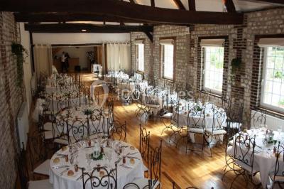 Salle de réunion avec des tables blanches, des chaises en osier et un écran de projection, dans un cadre en briques…