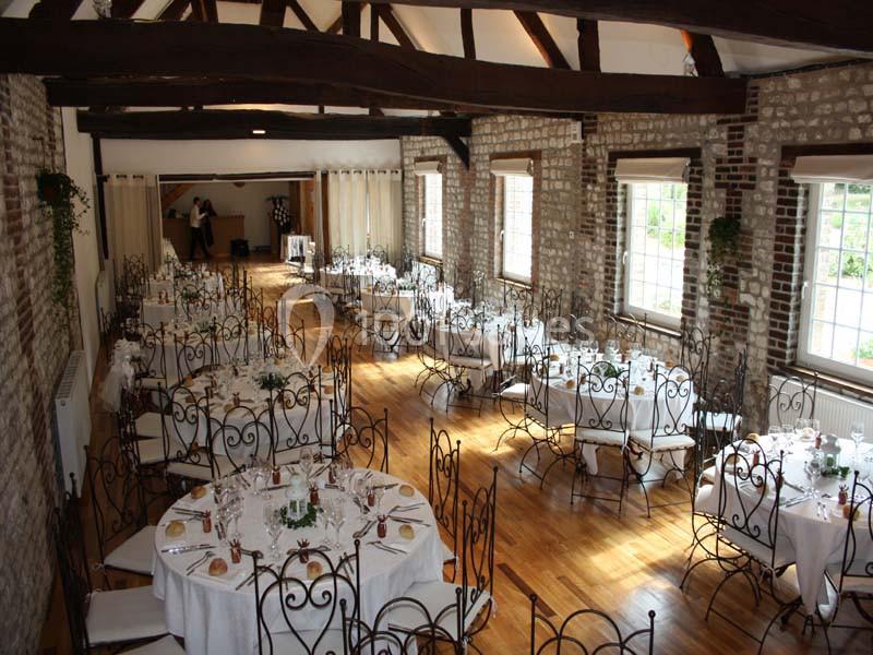 Salle de réception lumineuse avec murs en briques, poutres apparentes et tables rondes dressées pour un événement.
