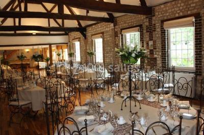 Salle de réunion avec des tables blanches, des chaises en osier et un écran de projection, dans un cadre en briques…