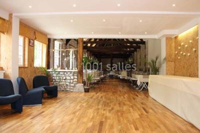 Salle de réunion avec des tables blanches, des chaises en osier et un écran de projection, dans un cadre en briques…