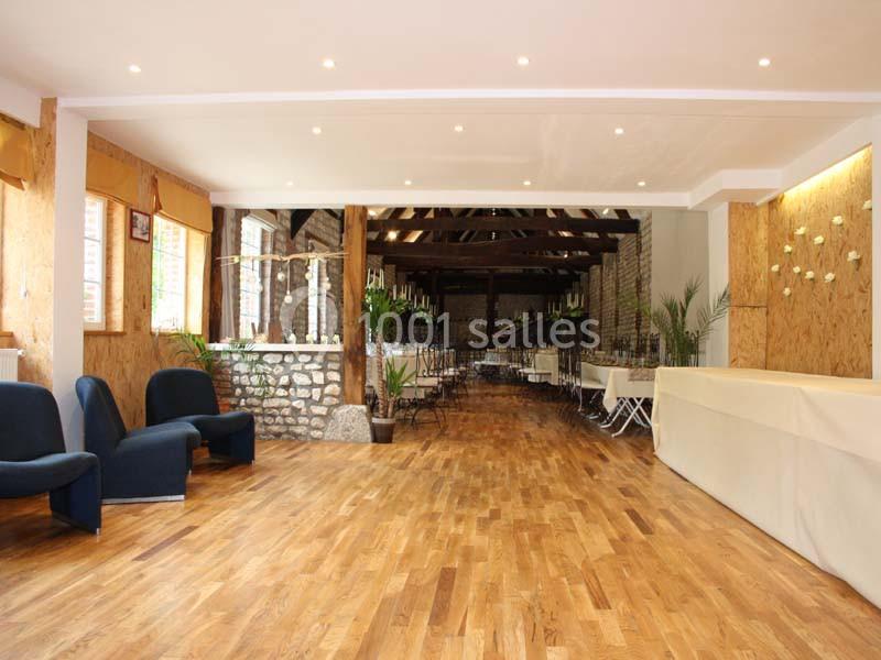 Salle lumineuse avec parquet en bois, murs en pierre et bois, chaises et tables alignées pour un événement.
