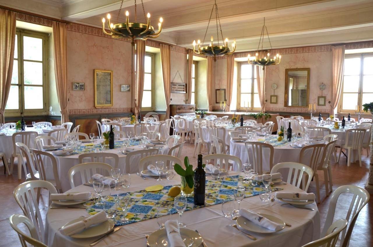 Salle de réception lumineuse avec tables rondes dressées, nappes blanches et décorations colorées.