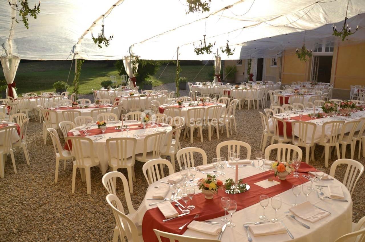 Tables rondes décorées pour un événement en extérieur sous une tente transparente, avec nappes blanches et chemins de table…