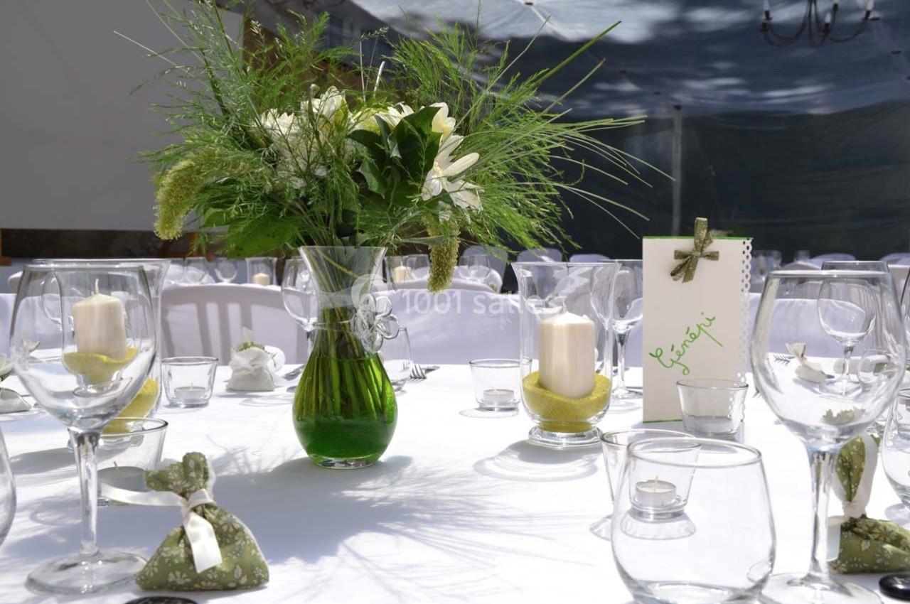 Table décorée pour un événement avec un bouquet de fleurs, bougies blanches et petits sachets cadeaux.
