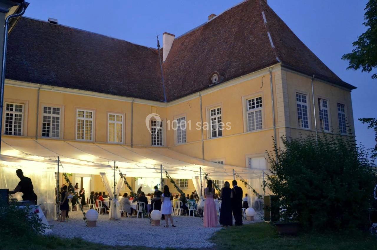 Façade éclairée d'un bâtiment ancien avec des invités rassemblés sous une tente lors d'un événement en soirée.