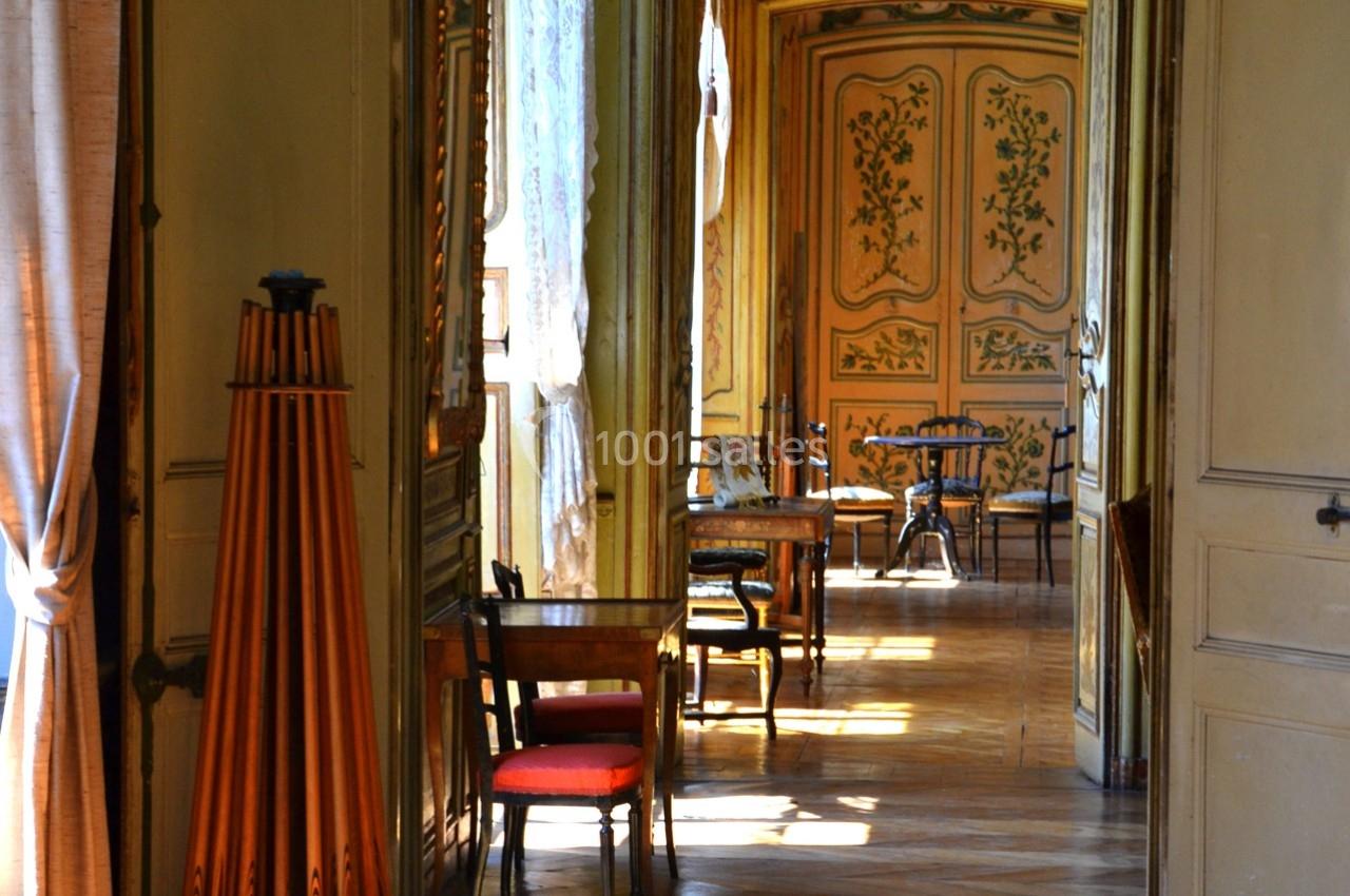 Intérieur d'un couloir lumineux avec parquet, meubles anciens et portes ornées de motifs végétaux.