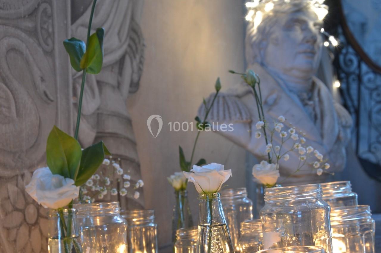Bougies allumées et fleurs blanches dans des vases en verre devant une statue en arrière-plan.