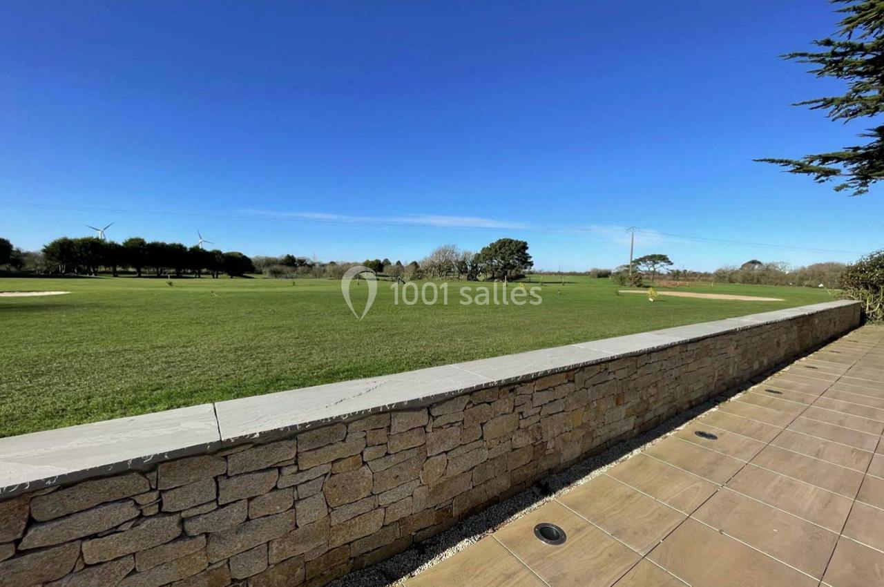 Vue d'un vaste espace vert avec une pelouse, des arbres, un mur en pierre et un ciel bleu dégagé.