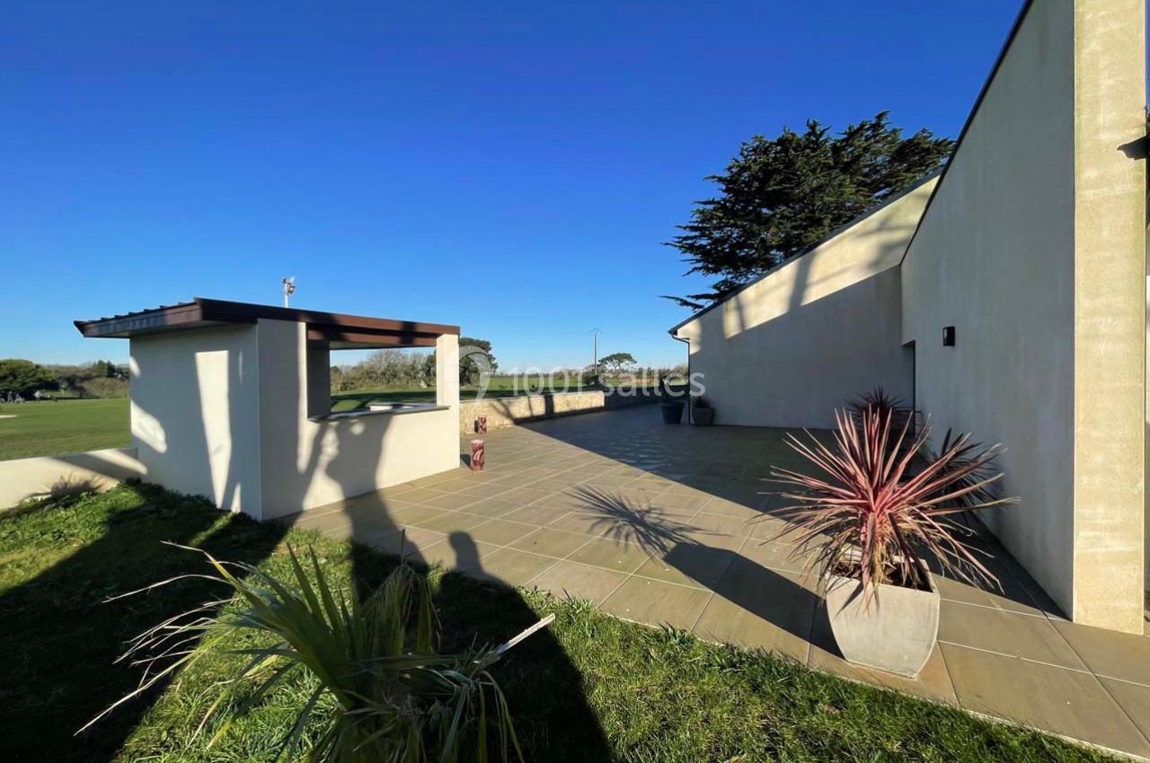 Terrasse ensoleillée avec carrelage beige, plantes en pots et vue dégagée sur un paysage champêtre.