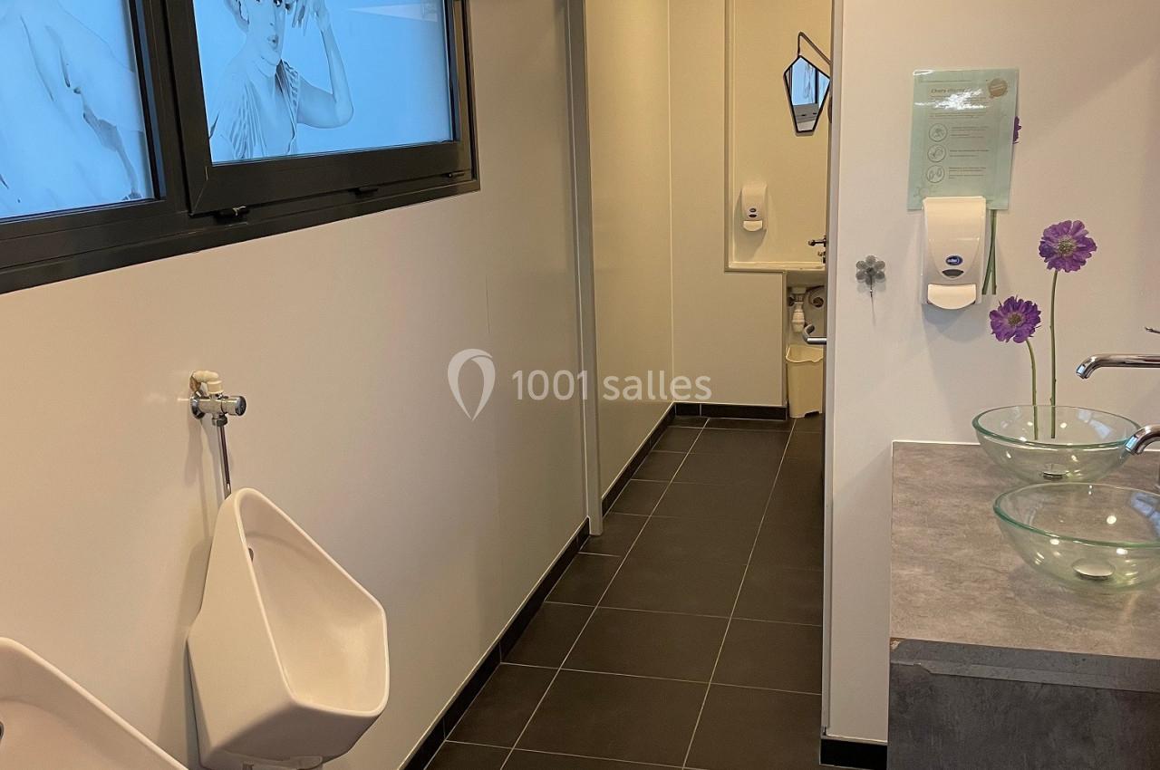 Salle de bain moderne avec urinoirs, lavabos en verre, distributeur de savon et décorations murales.
