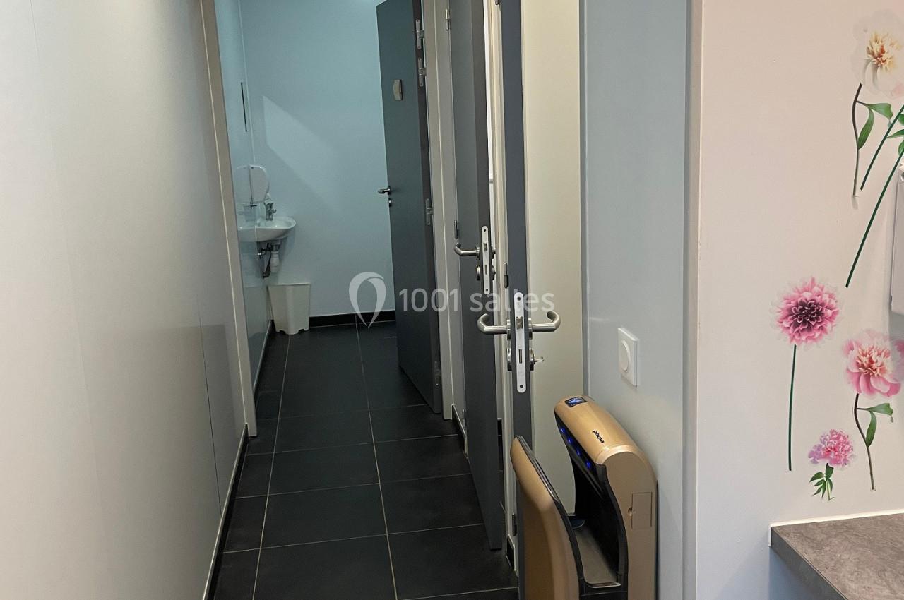 Couloir étroit avec sol en carrelage noir, portes ouvertes sur des pièces et décor floral sur un mur.