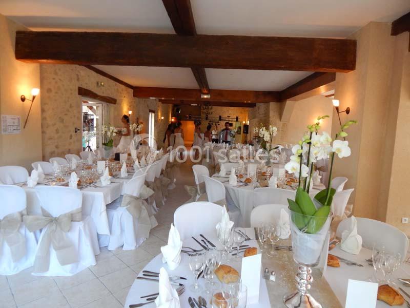 Salle de réception décorée avec des tables dressées, nappes blanches, orchidées et chaises ornées de nœuds.