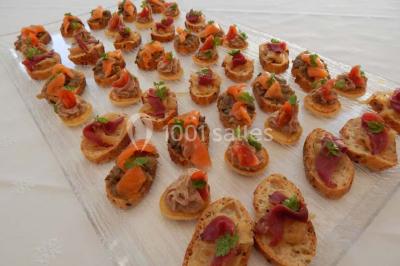 Façade d'une maison en pierre avec toit en ardoise, fenêtres symétriques et jardin clôturé au premier plan.