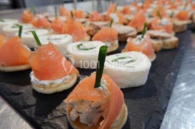 Façade d'une maison en pierre avec toit en ardoise, fenêtres symétriques et jardin clôturé au premier plan.