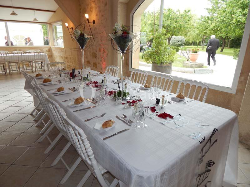 Table dressée pour un repas, avec nappes blanches, chaises alignées, décorations florales et vue sur un jardin extérieur.