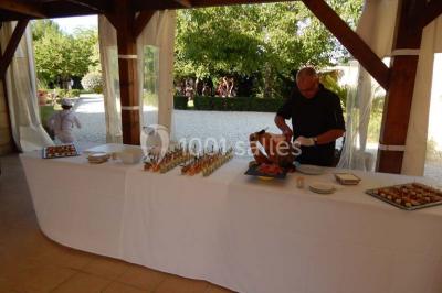 Façade d'une maison en pierre avec toit en ardoise, fenêtres symétriques et jardin clôturé au premier plan.