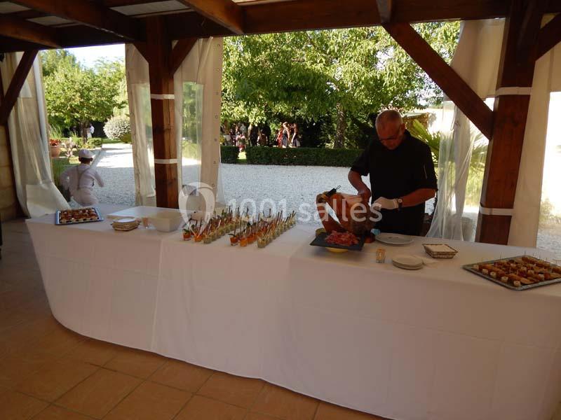 Un traiteur découpe un jambon sur un buffet en extérieur, entouré de verrines et d'amuse-bouches.