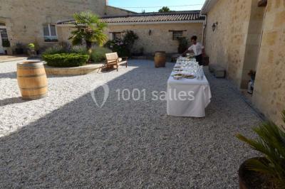 Façade d'une maison en pierre avec toit en ardoise, fenêtres symétriques et jardin clôturé au premier plan.