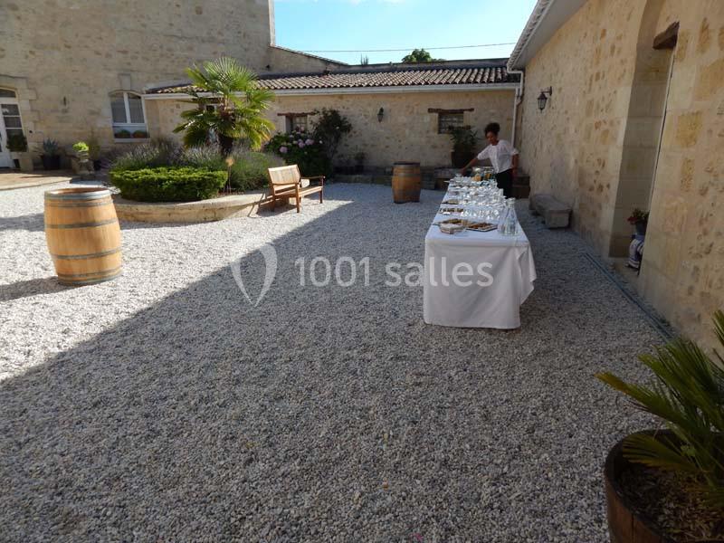 Table dressée pour un événement dans une cour en gravier entourée de murs en pierre et de végétation.