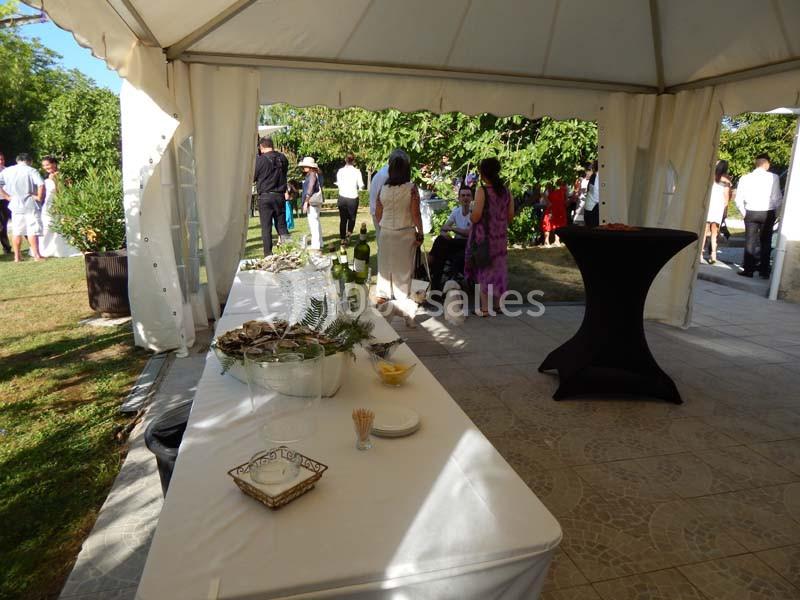Table de buffet dressée sous une tente blanche lors d'un événement en extérieur, avec des invités en arrière-plan.