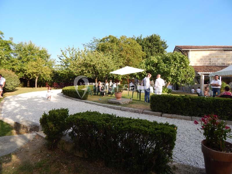 Personnes rassemblées dans un jardin avec des arbres, des tables sous des parasols et une allée en gravier.