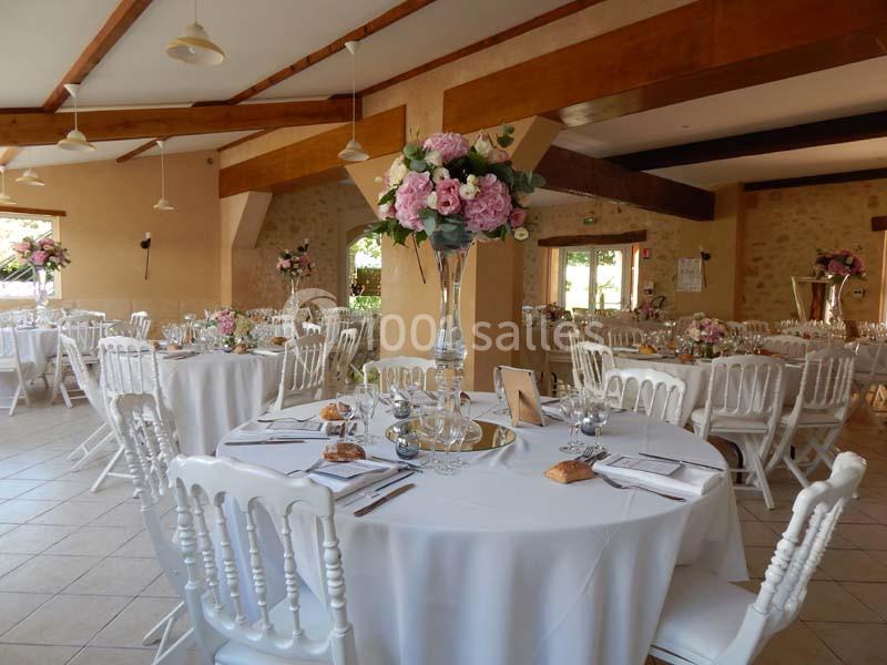 Salle de réception décorée pour un mariage, avec tables rondes, nappes blanches et centres de table fleuris.