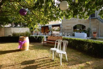 Façade d'une maison en pierre avec toit en ardoise, fenêtres symétriques et jardin clôturé au premier plan.