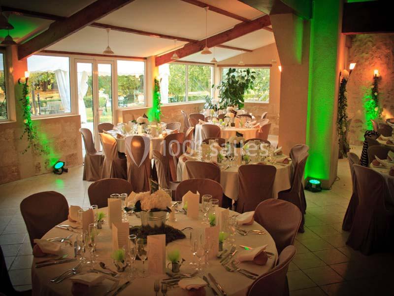 Salle de réception décorée pour un événement, avec des tables rondes dressées et une ambiance lumineuse chaleureuse.