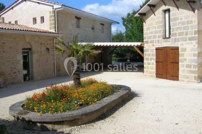 Façade d'une maison en pierre avec toit en ardoise, fenêtres symétriques et jardin clôturé au premier plan.