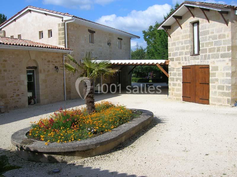 Cour en gravier avec un parterre fleuri central, entourée de bâtiments en pierre aux toits en tuiles.
