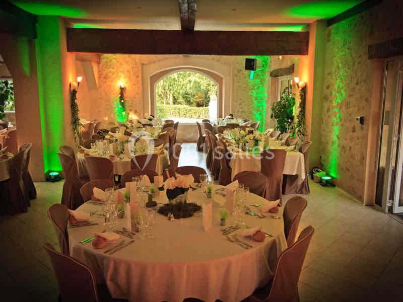 Salle de réception décorée avec des tables rondes dressées, éclairage chaleureux et vue sur un jardin.