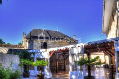 Façade d'une maison en pierre avec toit en ardoise, fenêtres symétriques et jardin clôturé au premier plan.
